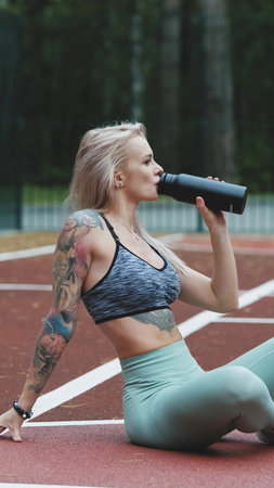 Concept of energy, vitality, well-being. Fit blonde in sportswear resting after training outdoors....