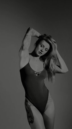 Blonde with a beautiful figure in a black bodysuit poses in the studio. Studio lighting, low...
