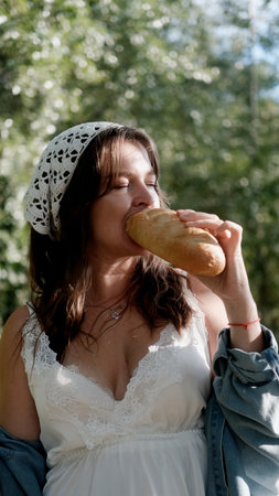 Portrait of a beautiful young woman in the countryside. The woman holds a loaf of bread and a bottle...