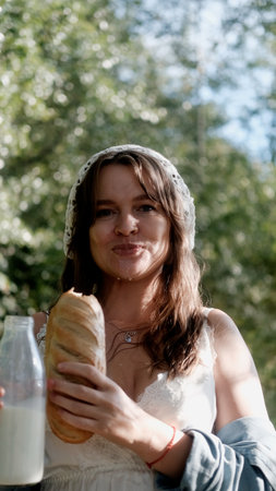 Portrait of a beautiful young woman in the countryside. The woman holds a loaf of bread and a bottle...