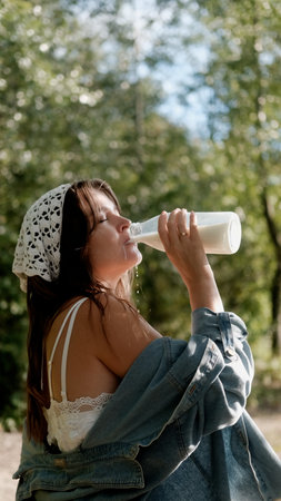Portrait of a beautiful young woman in the countryside. The woman holds a loaf of bread and a bottle...