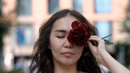 Beautiful woman covering part of her face with burgundy peony flowers. Natural beauty concept.