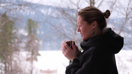Contented woman drinking hot tea and enjoying nature and breathing fresh mountain air during winter vacationの写真素材