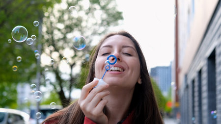 Young beautiful woman in burgundy coat blowing soap bubbles on city street. Freedom concept