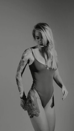 Blonde with a beautiful figure in a black bodysuit poses in the studio. Studio lighting, low exposure, monochrome light.の写真素材