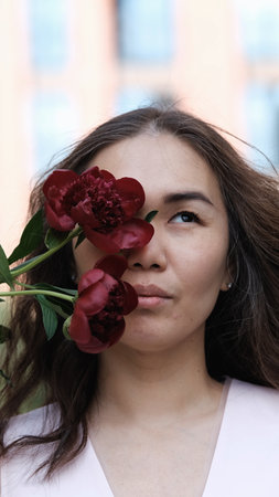 Beautiful woman covering part of her face with burgundy peony flowers. Natural beauty concept.