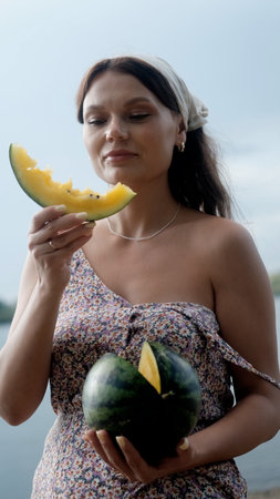 Young beautiful woman eating yellow juicy watermelon on the beach.