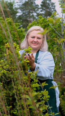 Portrait of happy female gardener standing among bright greenery of her garden