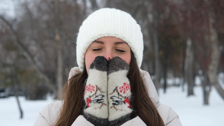 A portrait of a woman wearing a warm white knitted hat outdoors in winter. The young woman enjoys...
