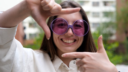 A cheerful and charming girl poses for the camera on a city street in the summer. The woman holds up a hand-made frame, like a photograph.の写真素材