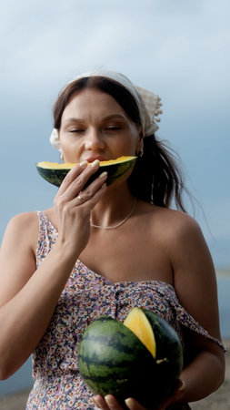 Young beautiful woman eating yellow juicy watermelon on the beach.の写真素材