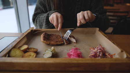 Pretty brunette enjoying tasty beef steak in restaurant in winter. Woman in warm cozy sweater eating meat near window. Snow outsideの写真素材
