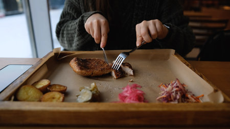 A woman enjoys a delicious meal in a restaurant in winter. The woman, wearing a warm, cozy sweater, eats the food by the window. A close-up of the woman's hands.の写真素材