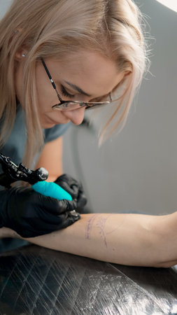 Close-up of a female tattoo artist creating a monochrome mountain range tattoo on a womans arm in a tattoo studioの写真素材