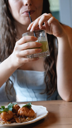 A close-up of a young woman with long curly hair drinking a cocktail through a straw at a bar. Beautiful female lips take a sip from a glass using a straw. A brunette samples a delicious drinkの写真素材