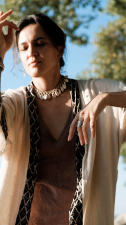 A beautiful brunette dressed in boho style meditates and dances in the forest. A magical ritual takes place against a green forest backdrop.の写真素材