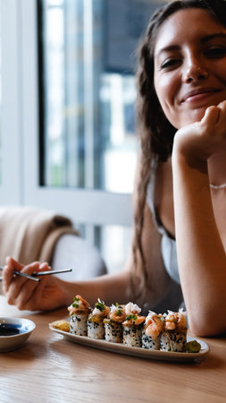 A girl eats Japanese sushi rolls with chopsticks, smiling with pleasure