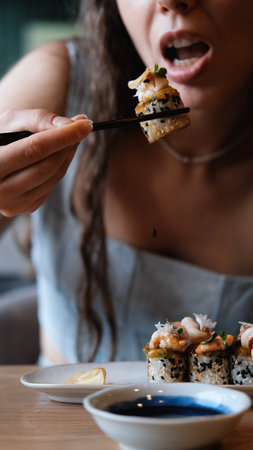 A beautiful girl eats Japanese sushi rolls with chopsticks, smiling with pleasureの写真素材