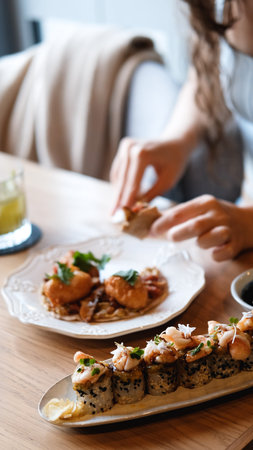 A beautiful girl eats Japanese sushi rolls with chopsticks, smiling with pleasureの写真素材