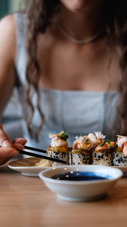 A beautiful girl eats Japanese sushi rolls with chopsticks, smiling with pleasureの写真素材