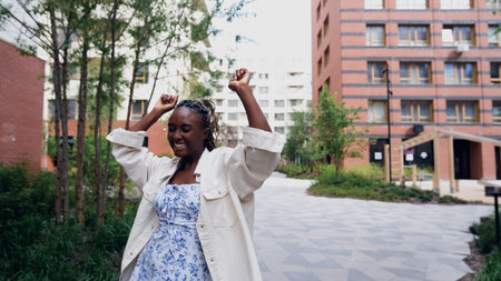 A young woman relaxes and unwinds while walking along a city street in a new eco-friendly residential complex. She dances to background music and laughs. Concept of relaxation and stress-free recreation.の写真素材