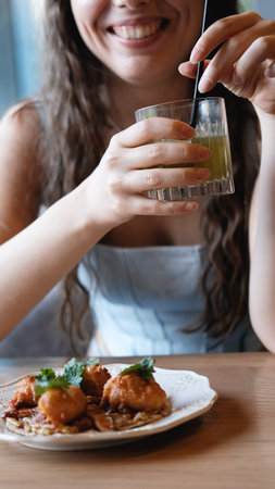 A close-up of a sweet young woman with long curly hair drinking a cocktail through a straw at a city bar. Beautiful female lips take a sip from a glass using a straw at a cafe. A brunette samples a delicious drinkの写真素材