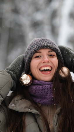 A beautiful young woman in winter clothes is happily spending her free time in a snowy forest. She enjoys the first snow. Active winter recreation.の写真素材