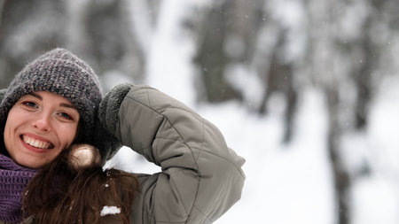 A beautiful young woman in winter clothes is happily spending her free time in a snowy forest. She enjoys the first snow. Active winter recreation.の写真素材