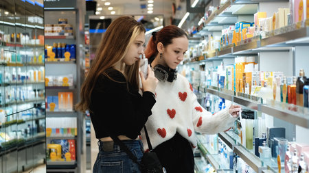 December 10, 2025. Russia, Novosibirsk. Young female shoppers and teenage girlfriends test cosmetics and fragrances in a perfume shop.のeditorial素材