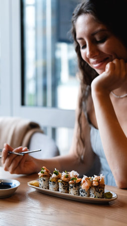 A beautiful girl eats Japanese sushi rolls with chopsticks, smiling with pleasureの写真素材