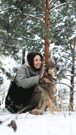 A young woman walks through a winter pine forest with her dog