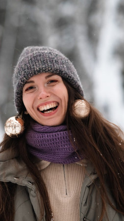A beautiful young woman in winter clothes is happily spending her free time in a snowy forest. She enjoys the first snow. Active winter recreation.の写真素材