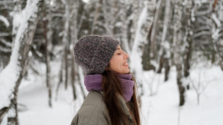 A beautiful young woman in winter clothes is happily spending her free time in a snowy forest. She enjoys the first snow. Active winter recreation.の写真素材