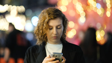 A beautiful girl holding a phone during a night walk through the city. Bokeh and lens flare effects...