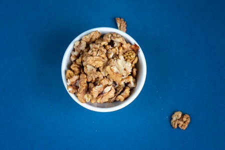 group of wallnuts in a white bowl is on a blue background, healthy food concept