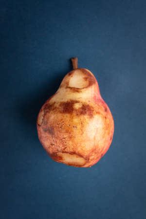 Over ripe red delicious pear against blue background. Zero waste and organic food conceptの写真素材
