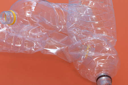plastic wrinkled bottle against orange background, environment pollution and recycling concept