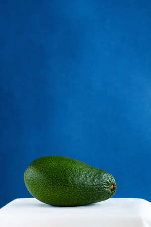 green fresh avocado on a white table against blue background, minimalistic picture with space for textの写真素材
