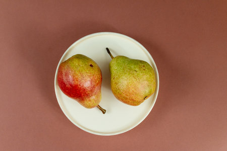 Two pears on white plate against brown background, top viewの写真素材