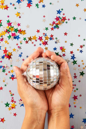 Hands holding disco ball on blue background with multicolored stars confetti