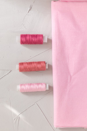 Needle and cotton fabric in pink color against gray background, slow fashion and home sewing concept