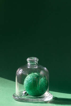 Green Christmas ball in glass jar against green background, natural sunlightの写真素材