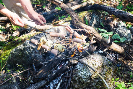 Cooking tasty sausages, bread and onion on campfire during hiking in the forest.の写真素材