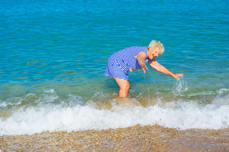 Happy elderly woman enjoying in waves of sea on the beach She feels delight and happiness.の写真素材