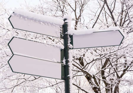 Arrow signboards covered by snow on winter forest background.