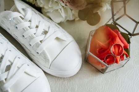 White wedding sneakers of the bride. Next to it is a bouquet and a box with wedding rings on red rose petals.の写真素材