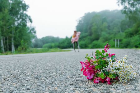 A bouquet of wild flowers on an asphalt road close-up. In the background, a blurry silhouette of a girl. Fogの写真素材