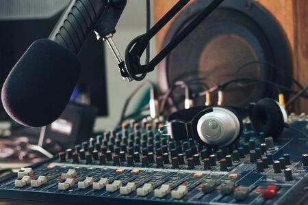 Microphone of the radio host in close-up, with the background of the mixing console, sound column and headphones. Radio Studioの写真素材