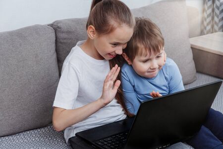Two children, a boy and a girl, are sitting on the sofa at home at a laptop