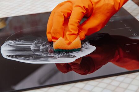 Close up hands cleaning kitchen glass ceramic electric surface with a sponge